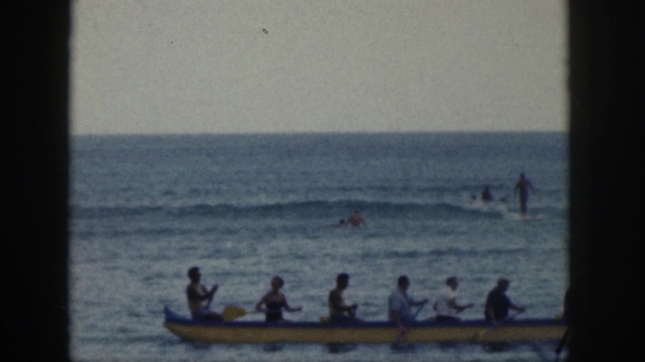 Yellow outrigger canoe with several paddlers moving across calm ocean water.
