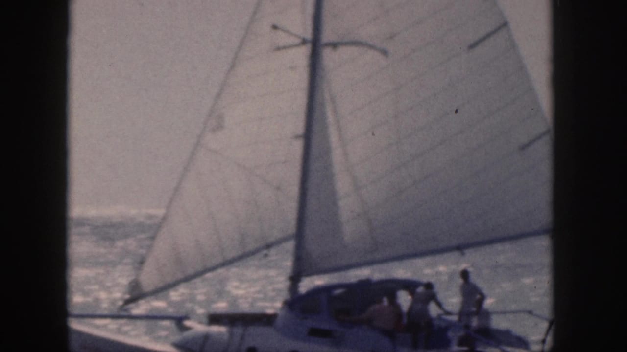 1959 Hawaii home-movie frame of a white catamaran moving across calm ocean water with people seated and standing near the cabin.
