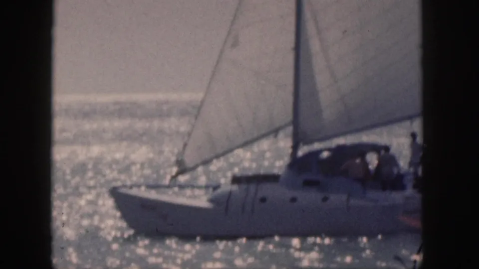 1959 Hawaii 8mm frame showing a side view of a white catamaran sailing past on shimmering ocean water with people aboard.