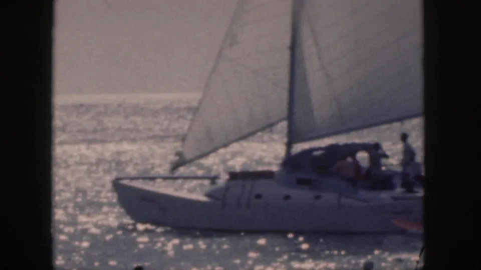 1959 Hawaii home-movie frame of a catamaran under sail, cropped at the edge as passengers remain visible near the cabin.