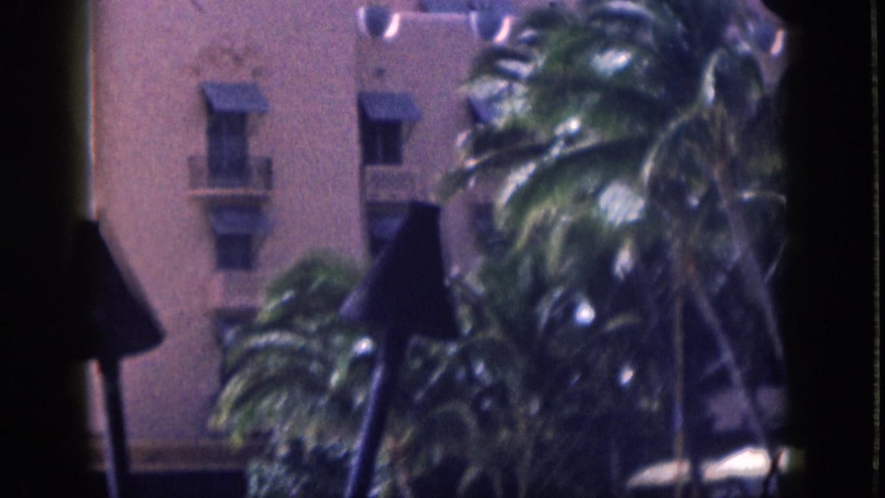 1959 Hawaii home-movie frame of palm trees in front of a pink stucco resort building, partly obscured by dark foreground shapes.