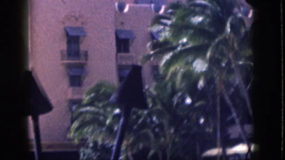 1959 Hawaii home-movie frame of palm trees in front of a pink stucco resort building, partly obscured by dark foreground shapes.
