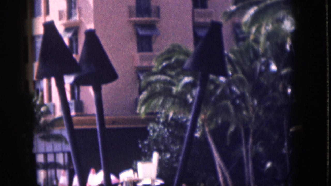 1959 Hawaii resort view with palm trees, dark triangular awnings, and a pink stucco building in soft 8mm color.