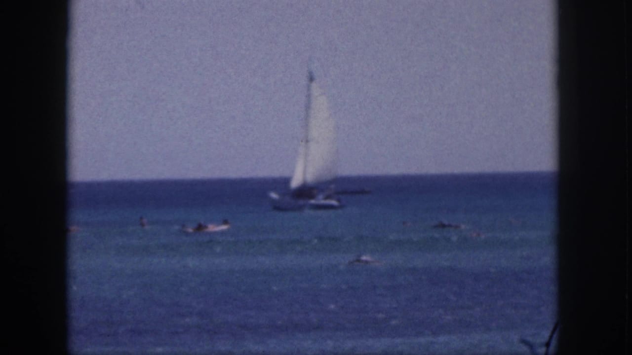 Small sailboat offshore with swimmers in calm blue water.