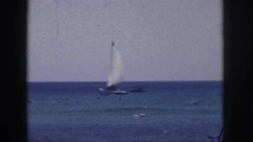 Soft 8mm Hawaii frame from 1959 showing a small sailboat and scattered swimmers in the sea.