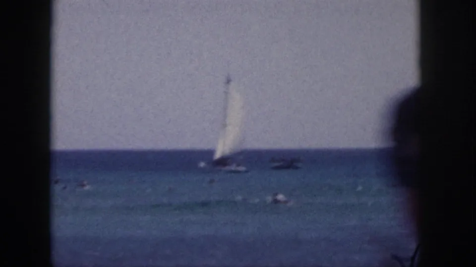 1959 Hawaii 8mm frame with an offshore sailboat, distant swimmers, and dark projector-like frame edges.