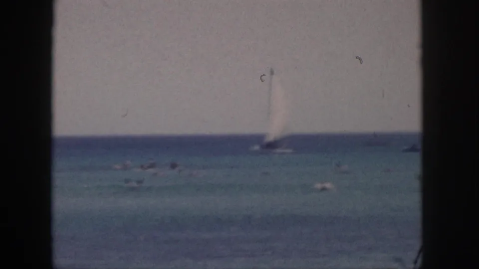 1959 Hawaii home-movie frame showing a sailboat near the horizon, small craft, and open water in muted color.
