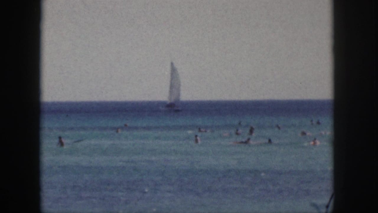 Swimmers in turquoise ocean water with a distant sailboat on the horizon.
