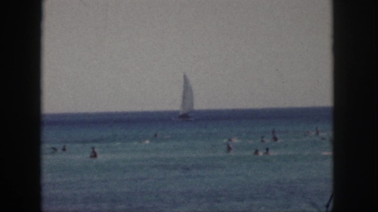 1959 Hawaii home-movie still with several distant swimmers and a sailboat against the blue horizon.