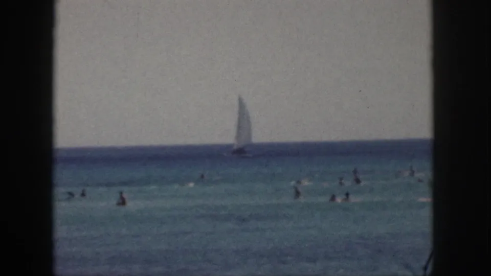 1959 Hawaii home-movie still with several distant swimmers and a sailboat against the blue horizon.
