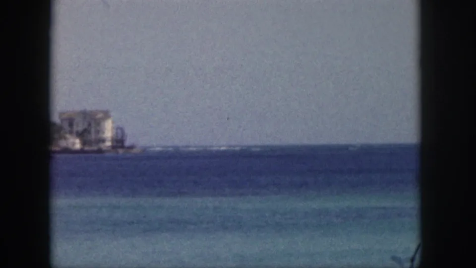 1959 Hawaii ocean view with a shoreline building at the left edge, pale sky, and blue water seen through window framing.
