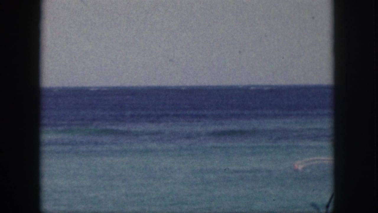 Distant paddler on blue-green water with a dark ocean horizon and black film borders.