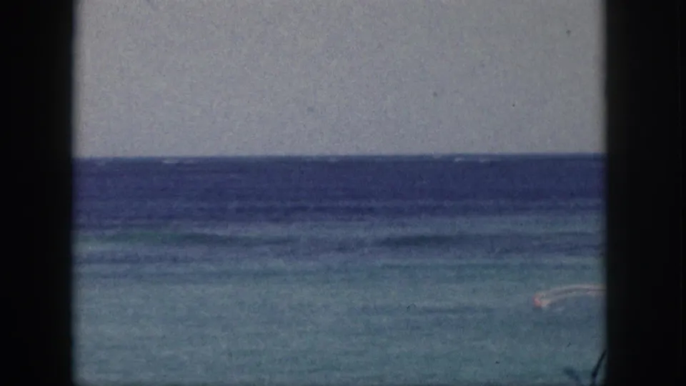 1959 Hawaii 8mm frame showing a distant person paddling on calm blue-green water beneath a pale sky.
