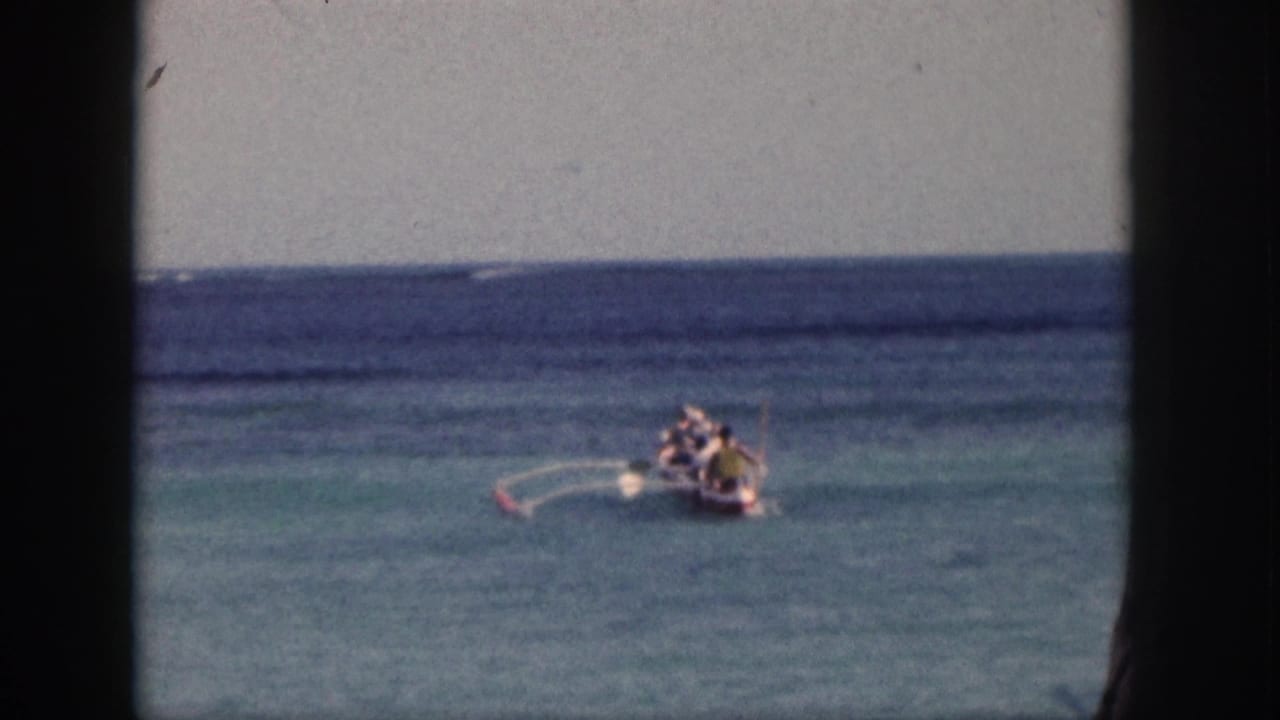 Small boat with people on turquoise ocean, framed by dark film borders.