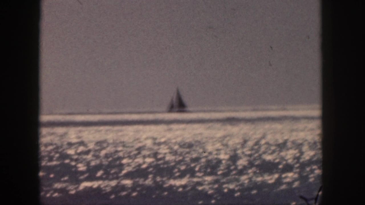 Distant sailboat silhouette on shimmering ocean beneath a hazy sky.