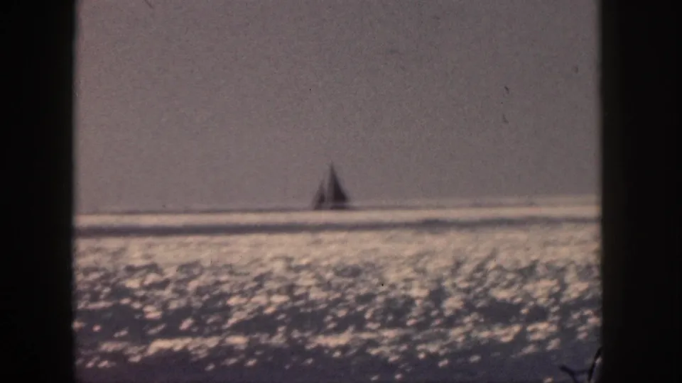 1959 Hawaii home-movie frame with a sailboat far offshore on bright, reflective water.