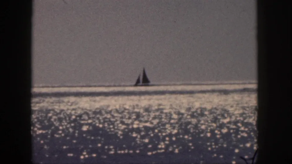 1959 Hawaii 8mm frame showing a distant sailboat against a hazy horizon and bright water reflections.