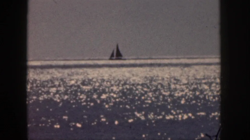 1959 Hawaii home-movie frame of a sailboat on reflective ocean water, seen through soft 8mm framing.