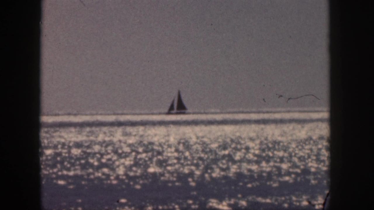 Distant sailboat on a bright ocean horizon with dark film borders.