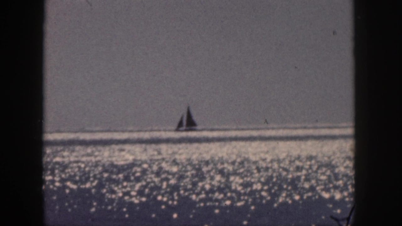 Small sailboat silhouetted near the horizon over glittering water.