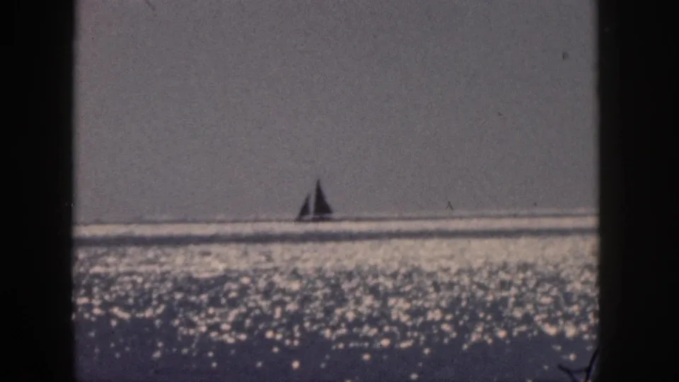 1959 Hawaii 8mm frame with a distant sailboat set against a hazy horizon and shimmering sea surface.