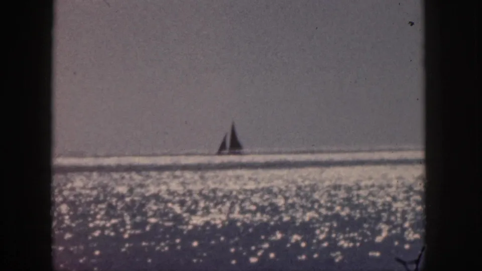 1959 Hawaii 8mm frame showing a lone sailboat near the horizon above a field of sparkling ocean reflections.