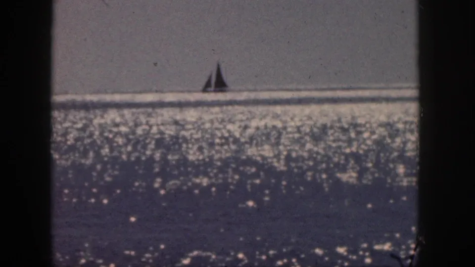 1959 Hawaii 8mm frame of a lone sailboat on the horizon, framed by soft grain, flicker, and bright ocean reflections.