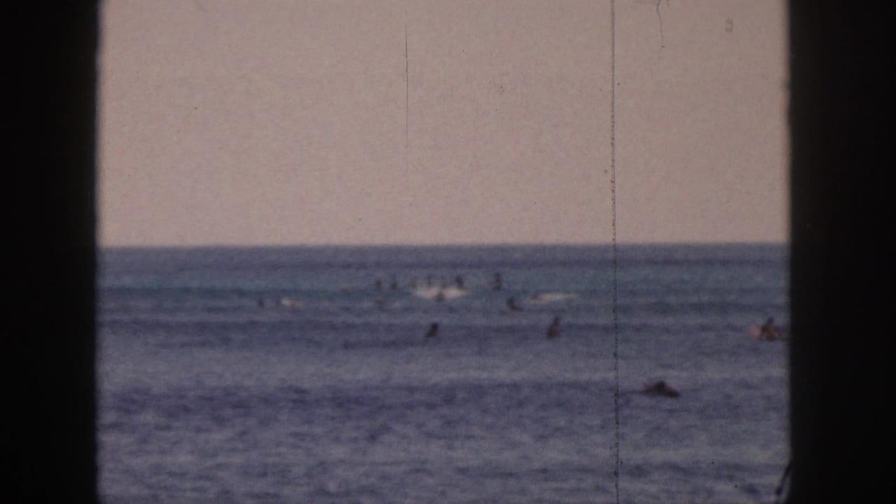 Distant 1959 Hawaii surf lineup with scattered surfers on boards across calm water, framed by dark side borders.