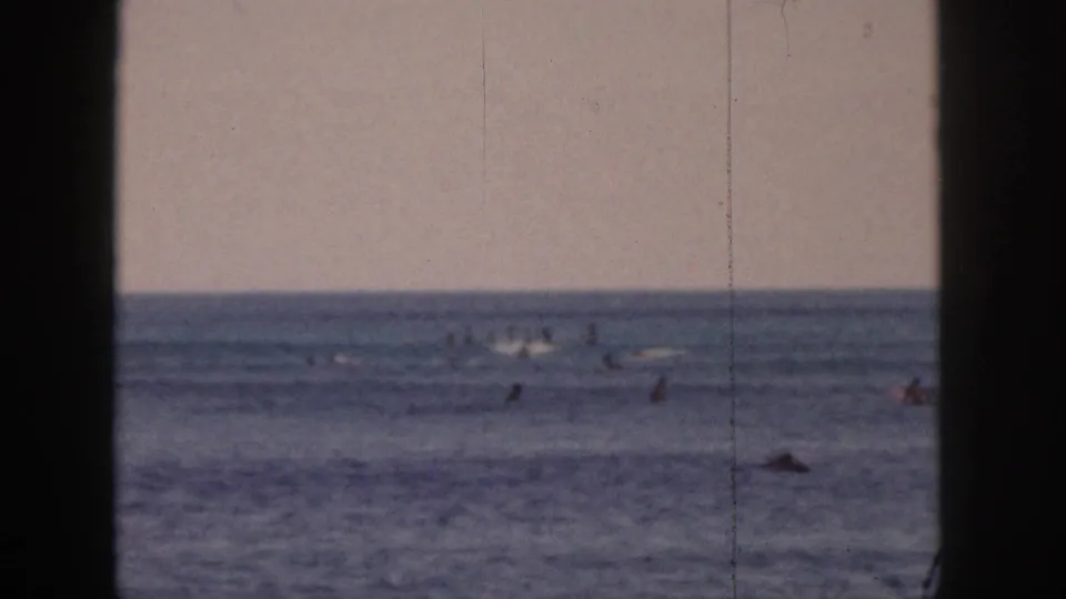 Distant 1959 Hawaii surf lineup with scattered surfers on boards across calm water, framed by dark side borders.