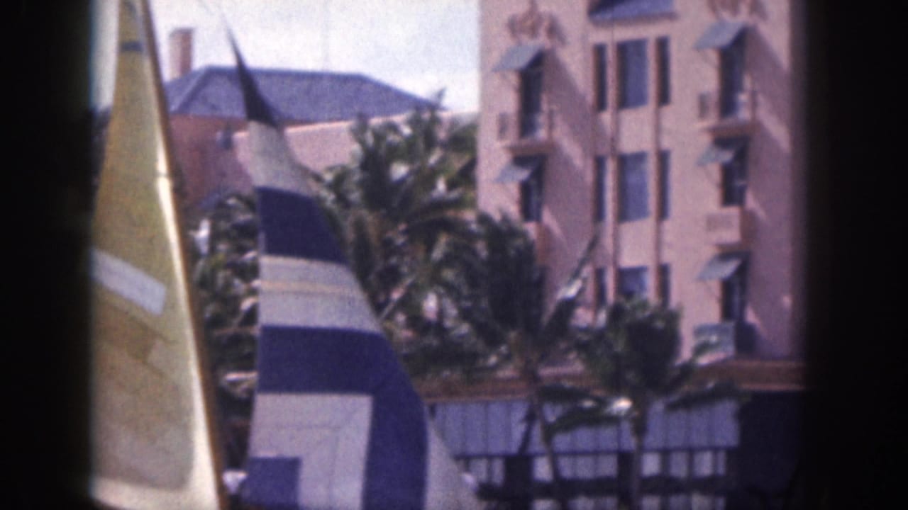 Sailboat sails and palm trees in front of a pink hotel exterior.