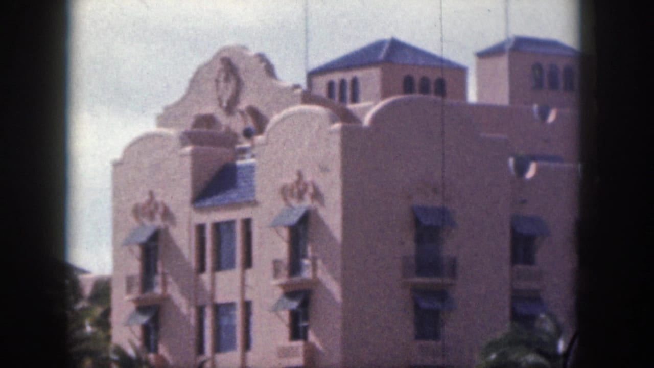 1959 Hawaii 8mm frame of an ornate pink hotel exterior with curved roofline details, windows, awnings, and palms.