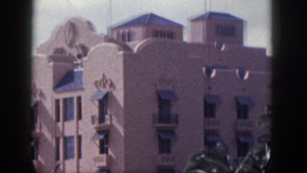 1959 Hawaii home-movie frame showing the upper stories of a pink resort-style building with arched windows and awnings.