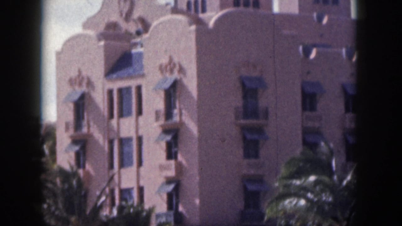 Pink multi-story building with arched details and palm trees in the foreground.