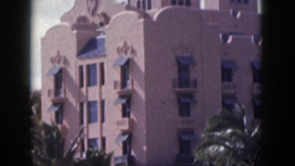 1959 Hawaii home-movie frame showing a pink resort-like building with arched windows, decorative roofline details, and palms.