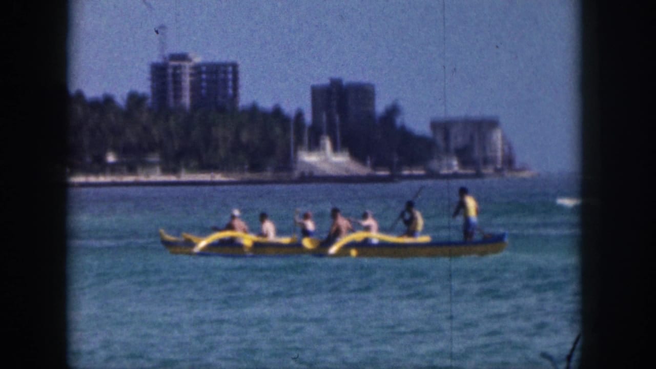 Yellow outrigger canoe carrying several people across blue water near a palm-lined shoreline.