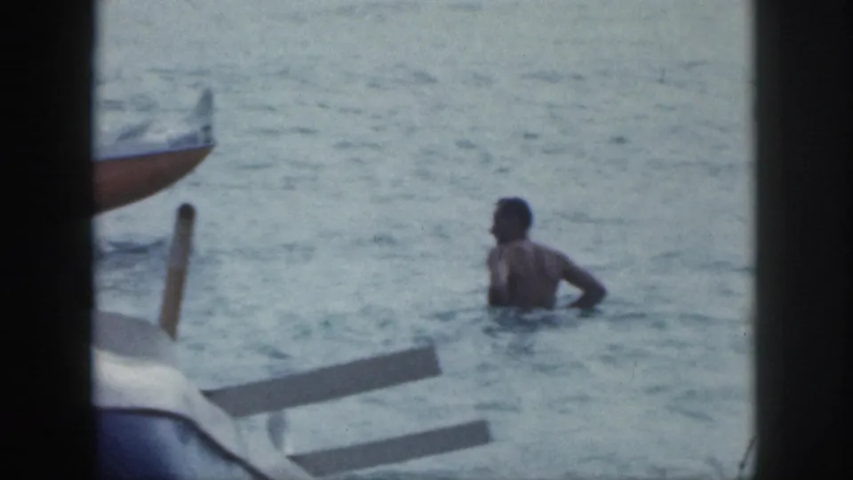 1959 Hawaii home-movie frame showing a man in the water beside visible outrigger canoe elements.