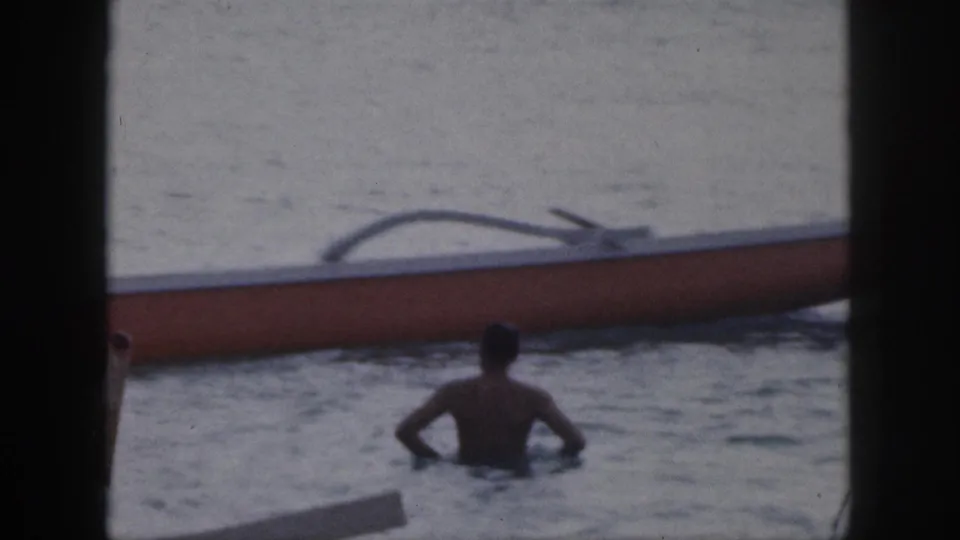 1959 Hawaii 8mm frame showing a swimmer in calm water beside an outrigger canoe, with dark film-frame borders.