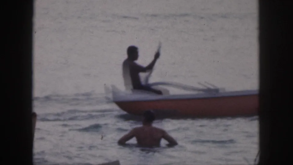1959 Hawaii 8mm frame with a silhouetted paddler seated in an outrigger canoe and a swimmer in the water.