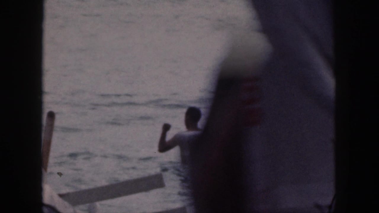 1959 Hawaii 8mm frame of a swimmer gesturing in the water beside an outrigger canoe, with heavy dark frame obstruction.