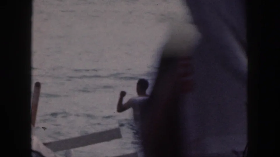 1959 Hawaii 8mm frame of a swimmer gesturing in the water beside an outrigger canoe, with heavy dark frame obstruction.