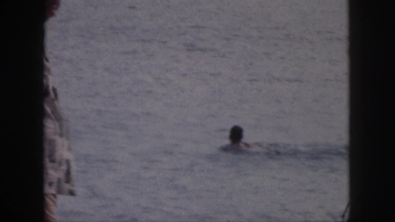 1959 Hawaii 8mm frame showing a swimmer in the ocean viewed through dark deck or window framing.