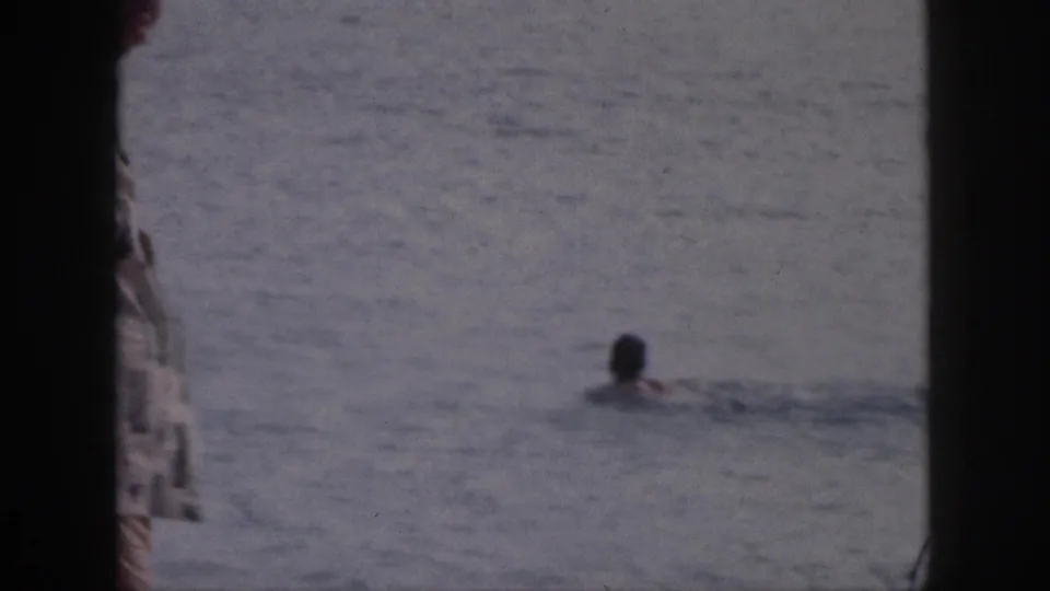 1959 Hawaii 8mm frame showing a swimmer in the ocean viewed through dark deck or window framing.