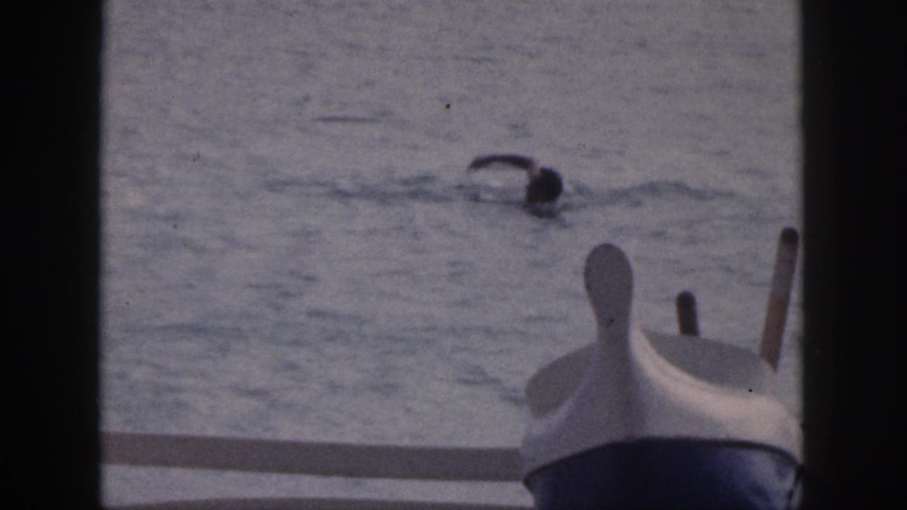 1959 Hawaii 8mm frame showing a swimmer mid-stroke near a small boat viewed from a deck.