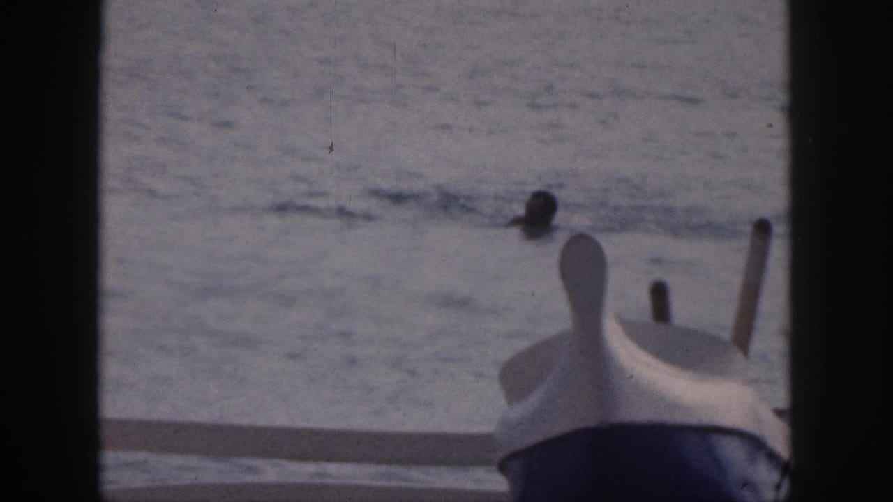 1959 Hawaii home-movie frame with a distant swimmer beyond the bow of a small boat in open water.