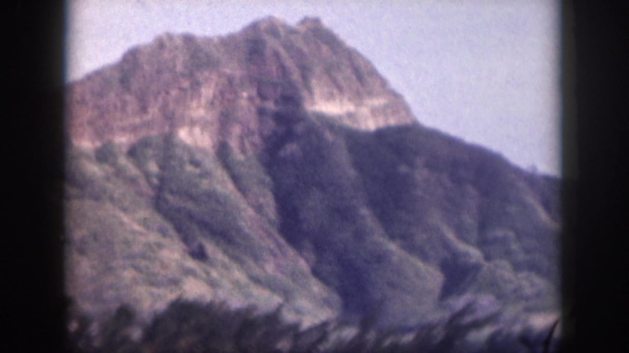 Mountain ridge with layered rocky faces and vegetation, framed by dark film edges.