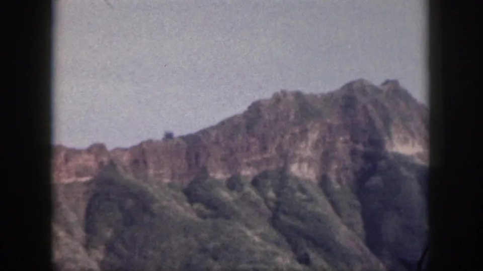 1959 Hawaii 8mm frame showing a rugged mountain ridge, green slopes, pale sky, and dark film borders.
