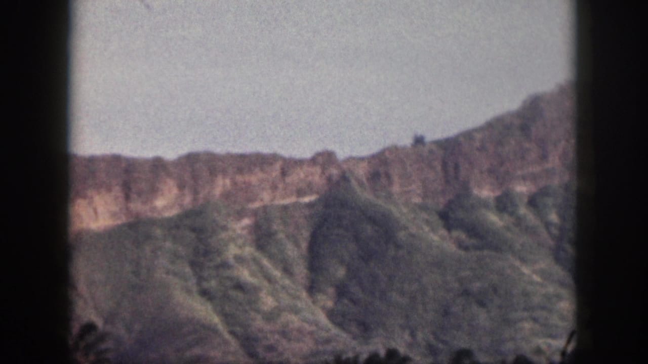 Vintage 8mm Hawaii frame showing a mountain ridge, green slopes, and dark film border during a landscape pan.