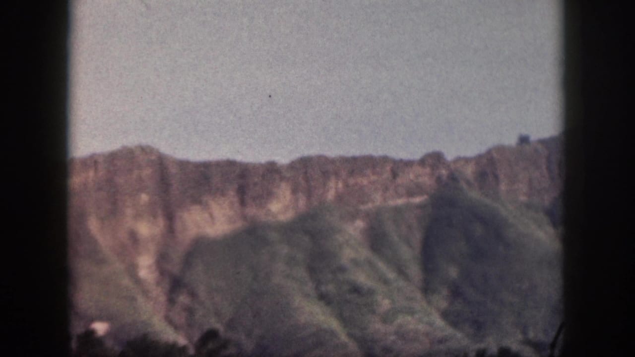 Soft 8mm view of green mountains and cliffs behind a dark vertical foreground edge.