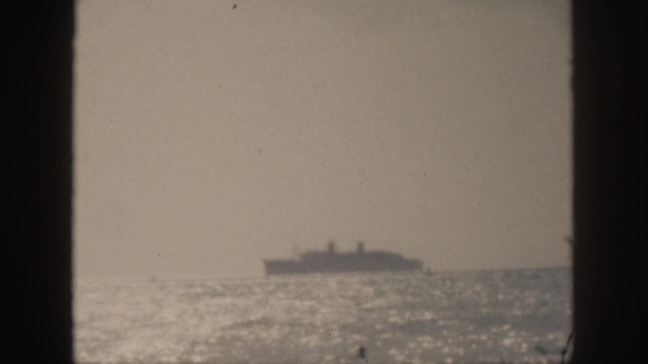 Distant ocean liner silhouetted on a hazy horizon behind dark frame edges.