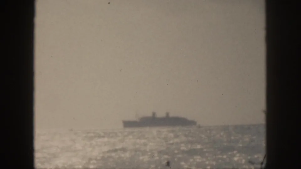 1959 Hawaii 8mm frame showing a distant ocean liner across shimmering water, partially bordered by dark vertical foreground edges.